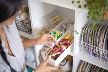 Female tailor choosing thread color for sewing clothes arrangement at box storage cupboard closeup