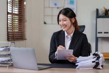 Obraz na płótnie Canvas Young Asian businesswoman who is happy to work in the office with a lot of paperwork arranged on the desk.