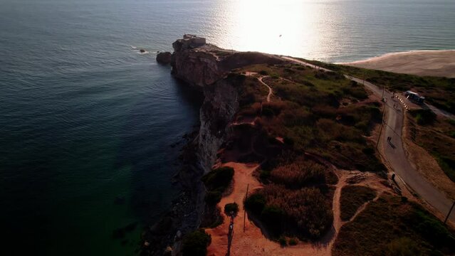 View of the lighthouse of Nazare. Coast of Portugal. Aerial contre jour drone footage of sea waves reaching shore.