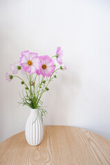 Fresh Pink Cosmos flowers in white vase. Seasonal flowers indoor decoration on wooden table. pink and white Cosmos.