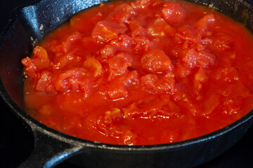 Cooking chopped tomatoes in a cast iron frying pan, on an electric hob stove