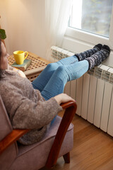 Woman heating feet on a chilly winter day, energy and gas crisis, cold room, heating problems.