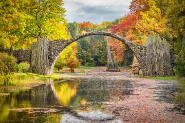 Rakotzbrucke bridge surrounded by autumn yellow trees in Rhododendron Park Kromlau, Saxony, Germany