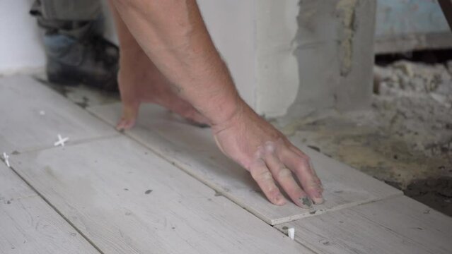 a man lays a white tile on the floor,work on laying ceramic tiles for the kitchen