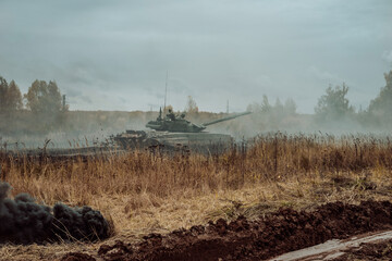 Heavy Military Tank on the battlefield at a hot spot. A tank moves through a field amidst...