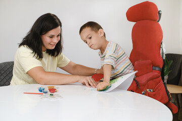 Child with cerebral palsy painting with fingers and hands boy that has health problems developing...
