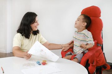 Child with cerebral palsy painting with fingers and hands boy that has health problems developing fine motor skills Education for children with mental, physical disorders, sensory art therapy