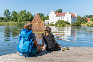 Sweden, Wanas – August 14, 2022: A mother and a kid are relaxing and contemplating in front of a beautiful ancient castle in front of a lake on a sunny summer day 