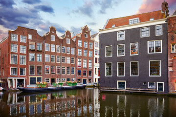 Naklejka premium Red-light district in Amsterdam city picturesque landscape panorama evening town with pink sunset sky. Traditional brick houses with windows ove water.