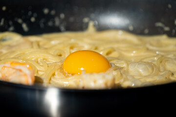 Close up macro to yolk in Creamy fried and boiled Spaghetti pasta in hot pan.