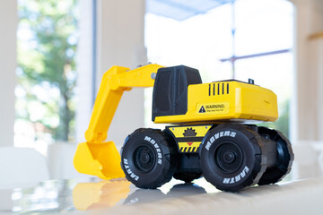 Backhoe loader, yellow construction toy vehicle with articulated parts built with sturdy plastic is placed on a table.