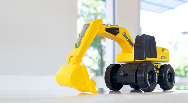 Backhoe loader, yellow construction toy vehicle with articulated parts built with sturdy plastic is placed on a table.