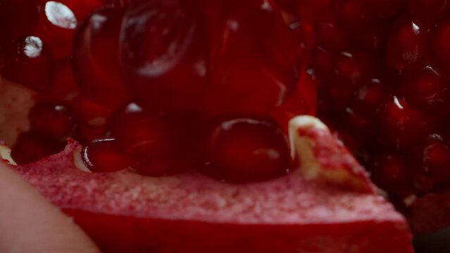 The girl picks out red grains from a pomegranate. Dolly slider, extreme close-up.