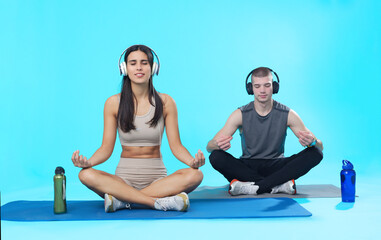 Young meditation couple; teenage man and woman sitting on mats in asana poses, listening to...