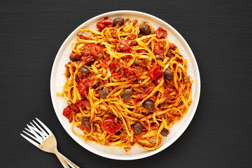 Homemade Tuna Linguine Pasta with Tomatoes, Olives and Capers on a Plate on a black background, top view. Overhead, from above, flat lay.