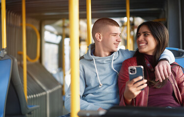 Couple sitting on a bus seat, looking at a phone, hugging and having good times browsing the internet while commuting - 539405458