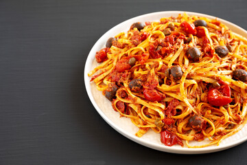 Homemade Tuna Linguine Pasta with Tomatoes, Olives and Capers on a Plate on a black background, side view. Copy space.