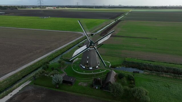 Traditional windmill in the polder in The Netherlands. Moving water in the rural land picturesque historical tourist attraction in europe. Aerial drone view.