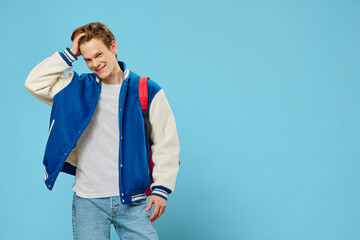 fashionable, stylish guy-student posing standing with a backpack on his shoulder on a blue...