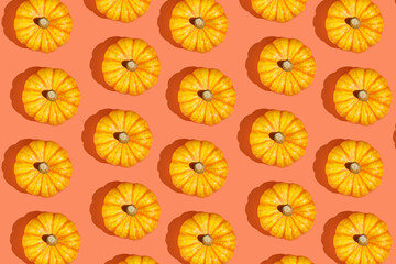 A hard light pattern of a small yellow decorative pumpkin on a bright orange seamless background, top view