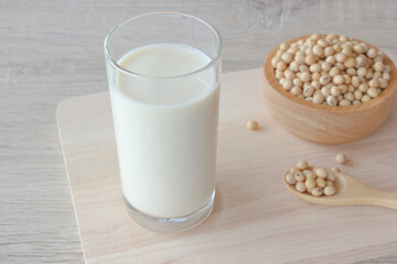 Glass of soy milk and soy beans in a bowl and spoon on wooden background.