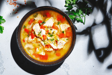 Warming autumn soup with red lentils, chicken fillet, vegetables, spices and paprika, comfort food. White table, hard light with leaf shadows, top view