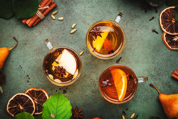 Mulled Cider glass cups: apple, pear and orange flavored hot cider with spices. Fermented low alcohol cocktail  fruit drink on green table with leaves, top view
