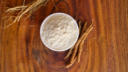 Roots and powder of Ashwagandha known as Withania somnifera in white bowl on wooden background. Indian ginseng, poison gooseberry, or winter cherry. Herbal adaptogen ayurvedic medicine.