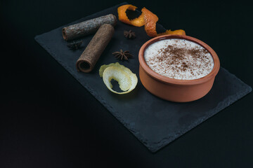 Rice pudding dessert served in an earthenware dish on a slate table accompanied by lemon and orange peel and cinnamon sticks. Foodie