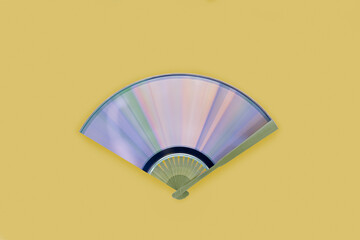 Traditional hand holding fan with compact disc with rainbow reflections. Diffraction of light into...