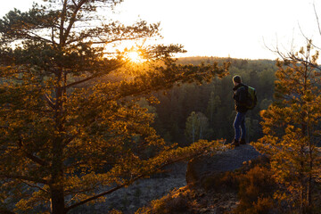 A man with a backpack standing on a rock in the forest at sunset. - Powered by Adobe