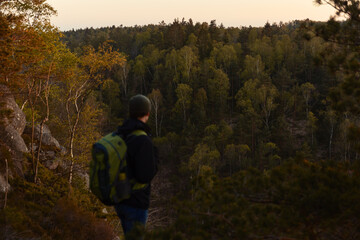 A man with a backpack standing on a rock in the forest at sunset.
