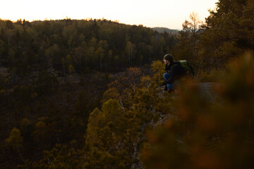 A man with a backpack standing on a rock in the forest at sunset