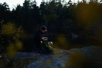 A caucasian man with a headlamp sitting on a rock by a lake in a forest at night. © Francis