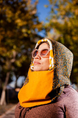 Outdoor fashion portrait of young Latin American woman with sunglasses, colourful headscarf, posing in park