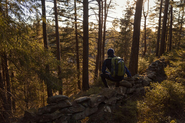 A caucasian man hiking in the forest sitting on a wall of rocks
