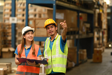 Two warehouse workers in hardhat and reflective jacket standing between rows of tall shelves at retail warehouse