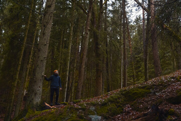 A caucasian man with a backpack standing next to a pine tree in a forest on a rainy day.