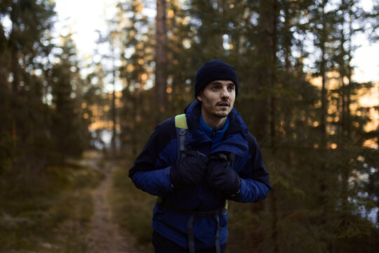 A caucasian man with a backpack walking on a forest path at sunset.