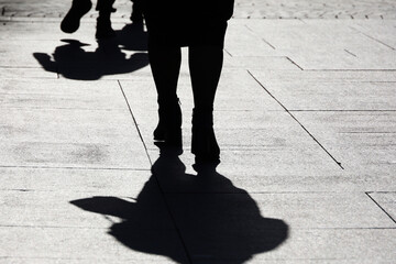 Silhouette of woman in autumn clothes walking down the street, black shadow on pavement. Concept of...