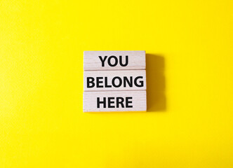 You belong here symbol. Wooden blocks with words You belong here. Beautiful yellow background. Business and You belong here concept. Copy space.
