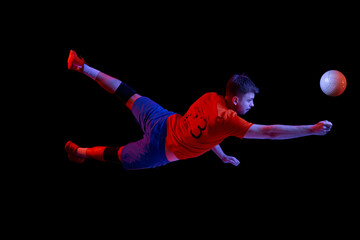 Young man, professional volleyball player in sports uniform in jump with ball isolated on dark background. Sport, action, healthy lifestyle, team sport