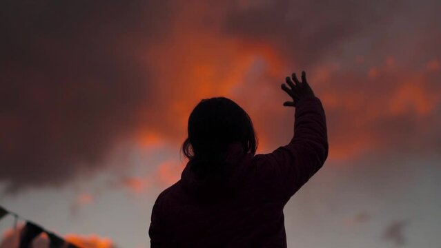 Sunset silhouette of Indian girl raised her hand towards sky in search of hope and faith. Hope concept in teenagers. Hopelessness in a woman.