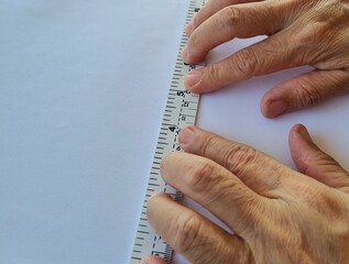 Close-up photo of hand holding a plastic ruler to help work on white paper