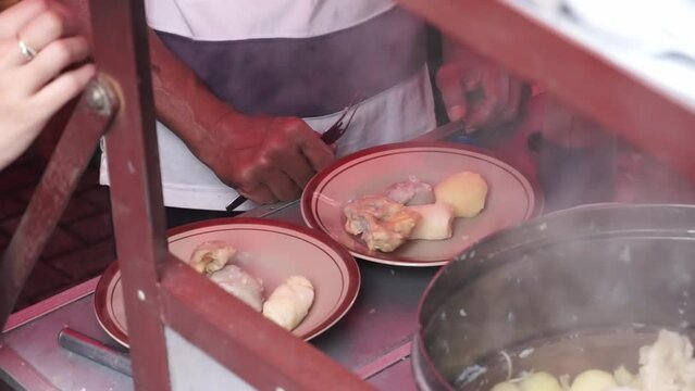 An Indonesian man street food vendor serves a customer in outdoor market. A man preparing a dish called 'Batagor' to customer on the street of Malang.