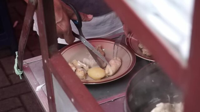 An Indonesian man street food vendor serves a customer in outdoor market. A man preparing a dish called 'Batagor' to customer on the street of Malang.