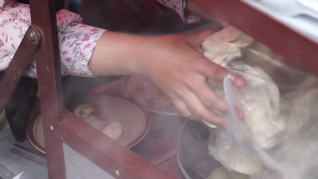 An Indonesian man street food vendor serves a customer in outdoor market. A man preparing a dish called 'Batagor' to customer on the street of Malang.
