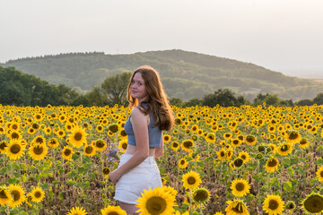 Fototapeta na wymiar Teenage girl on a sunny summer afternoon in a sunflower field, copy space