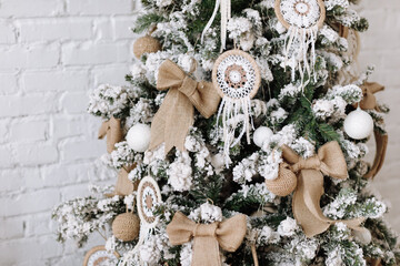 Fir tree decorated with Scandinavian style Christmas white balls and natural baubles. Christmas tree with dream catcher, burlap bow, snow. Merry Xmas and Happy Holidays, greeting card, New Year. Noel