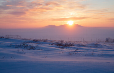 Winter arctic landscape. Industrial structures, electrical pylons and a satellite dish in the winter snow-covered tundra in the Arctic. Sunset over the tundra and mountains. Chukotka, Siberia, Russia.
